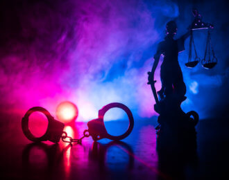 Legal law concept. Silhouette of handcuffs with The Statue of Justice on backside with the flashing red and blue police lights at foggy background.