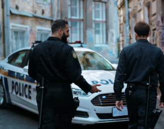 Two young men cops sit in patrol car walk pistol run enforcement happy officer police uniform auto safety security communication control policeman close up slow motion